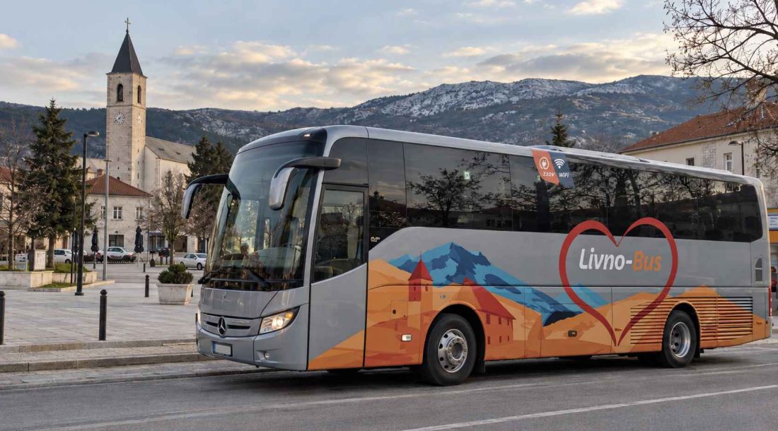 Autobus Livno-Busa u Tomislavgradu, s gradskim znamenitostima i planinama u pozadini.