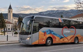 Autobus Livno-Busa u Tomislavgradu, s gradskim znamenitostima i planinama u pozadini.