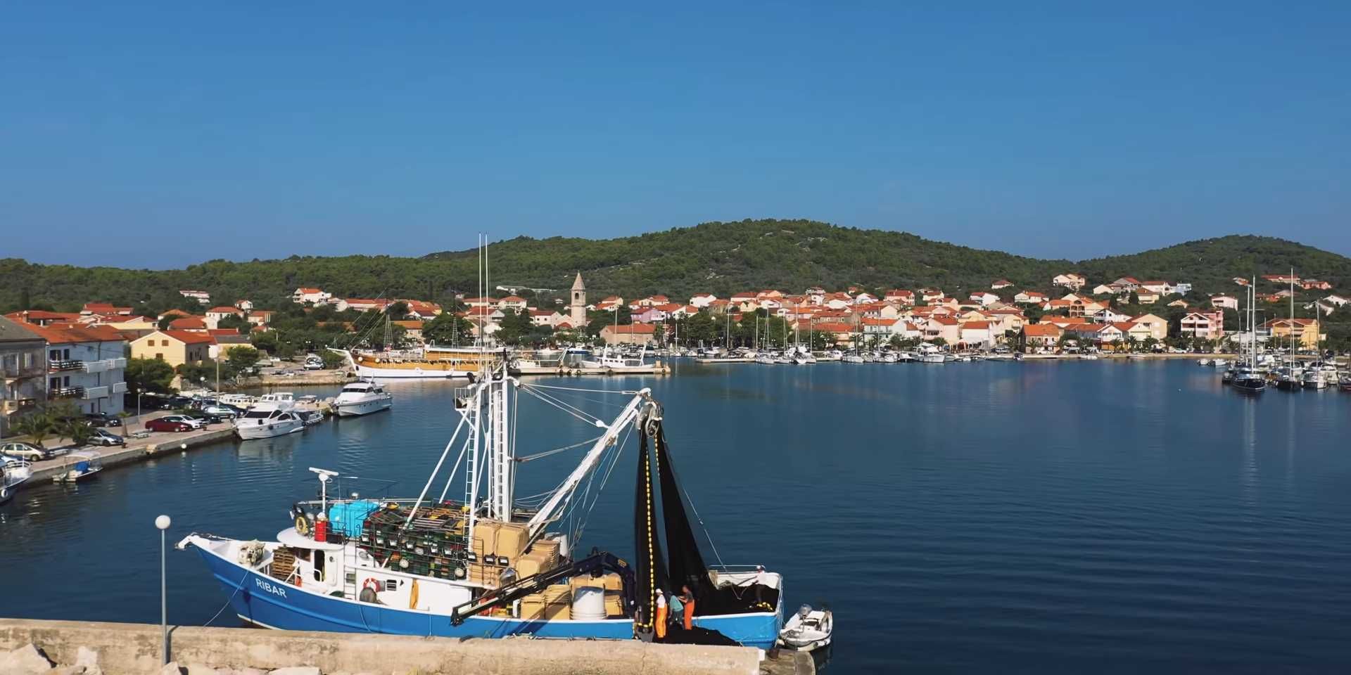 Ribarski brod u luci na Ugljanu s pogledom na obalno mjesto i brojne jedrilice.