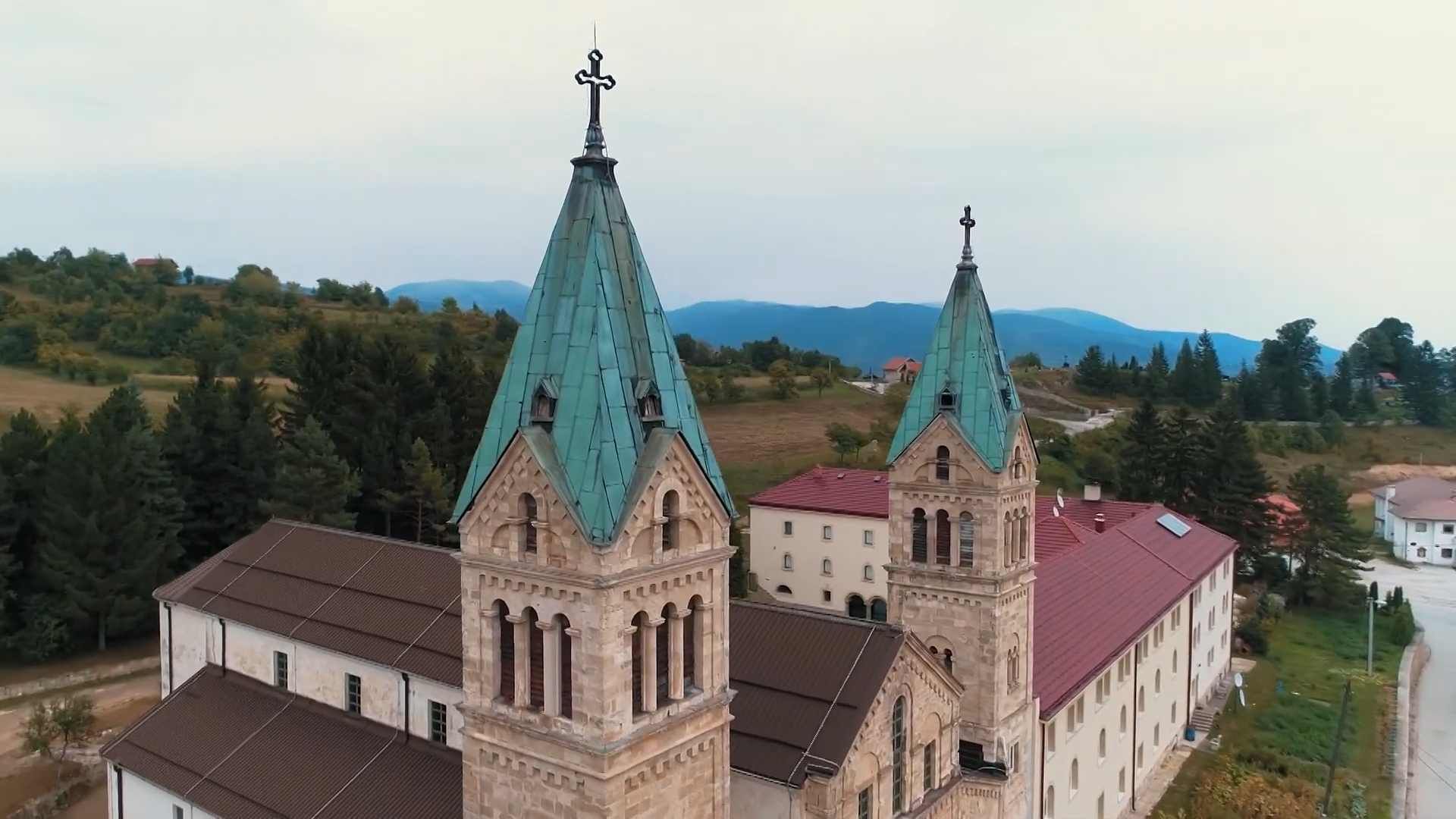 Pogled iz zraka na franjevački samostan Guča Gora s dva zvonika i zelenim krovovima.