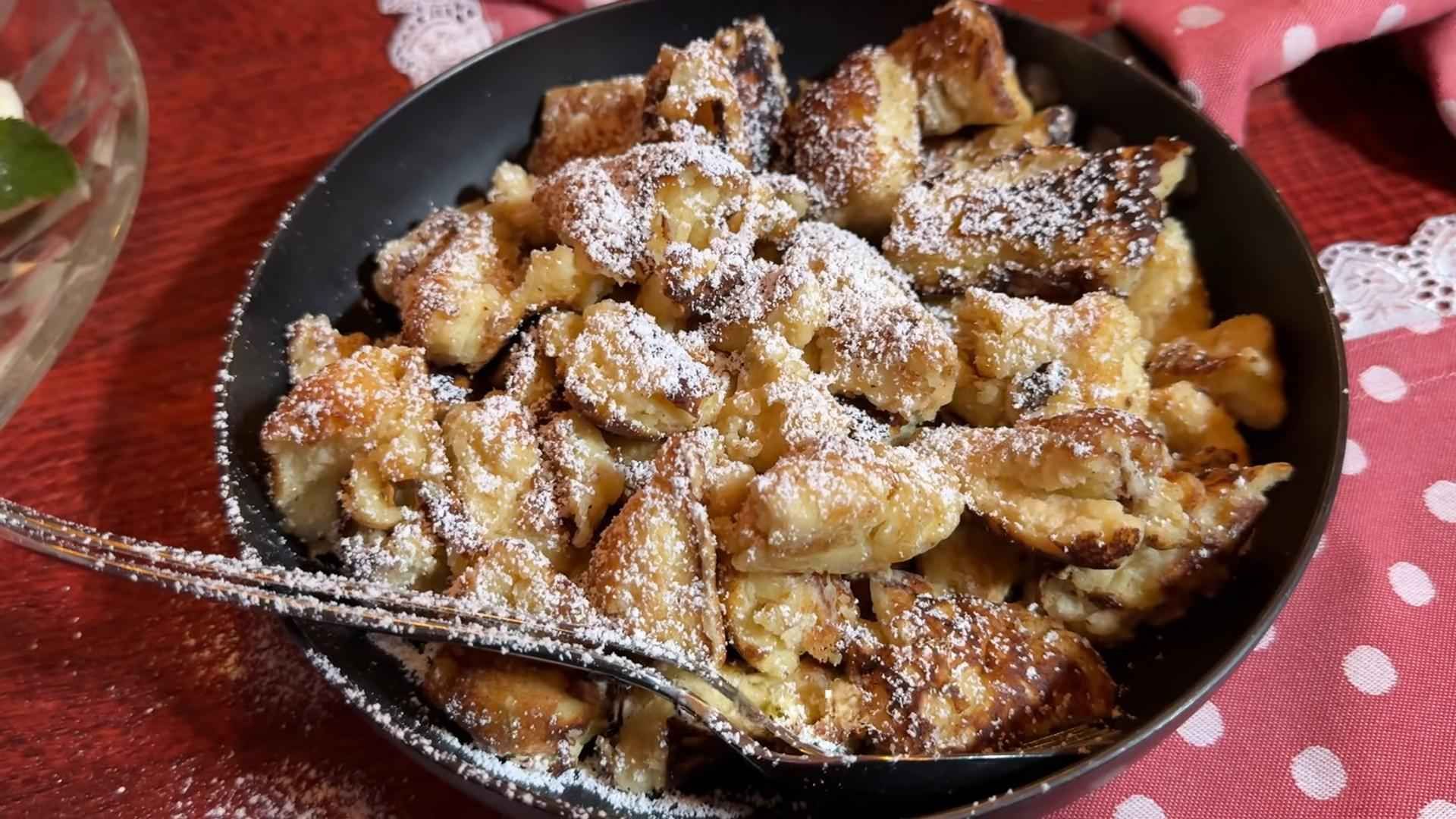 Komadi slatkog tijesta posuti šećerom u prahu u crnoj tavi.