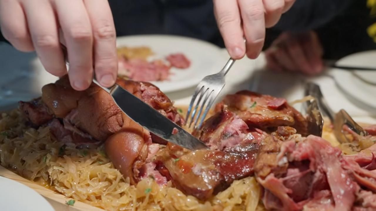 Osoba reže komade pečenog mesa posluženog na velikom pladnju s kiselim kupusom.