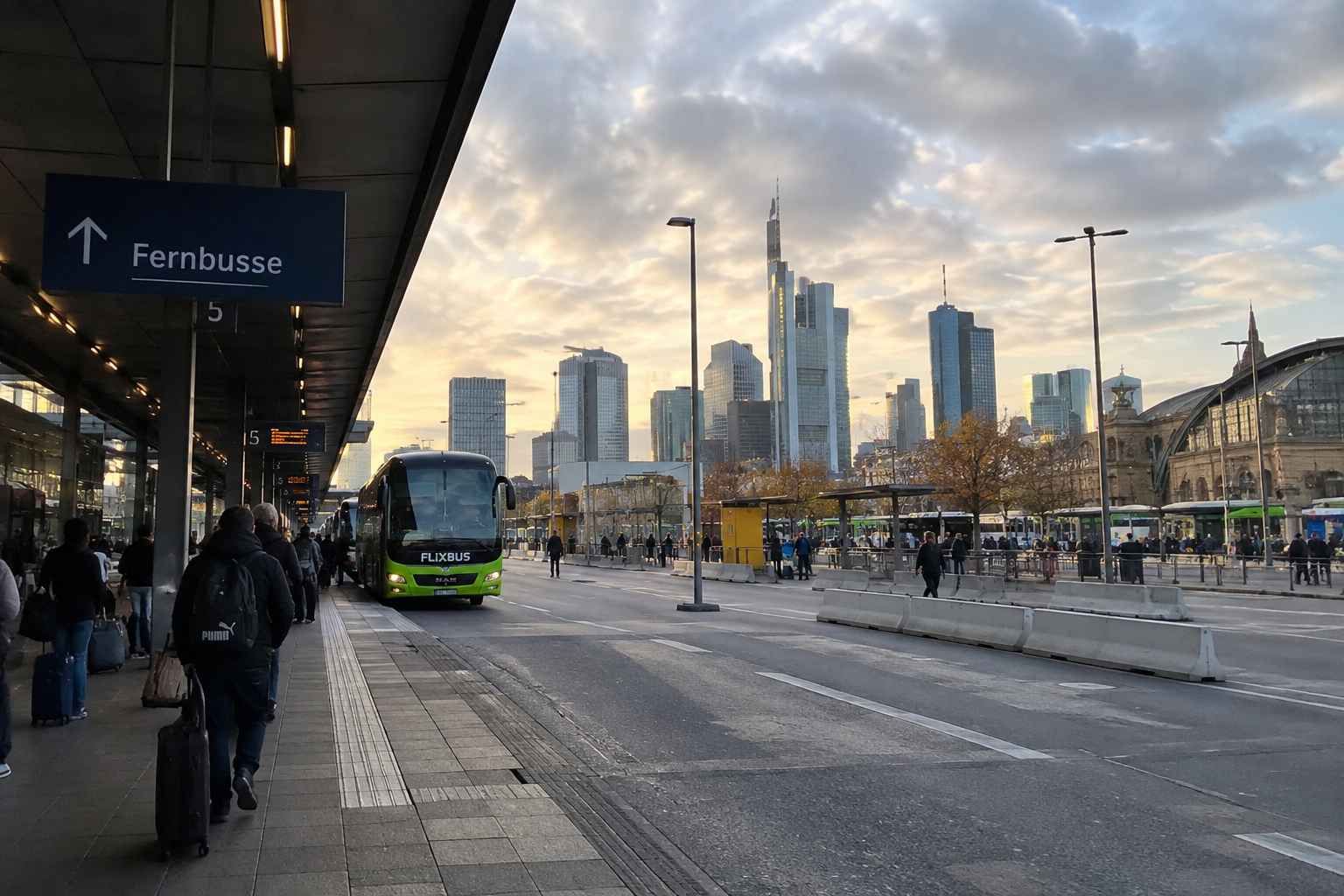 Međugradski autobusni kolodvor u Frankfurtu s autobusima, putnicima i neboderima u pozadini.
