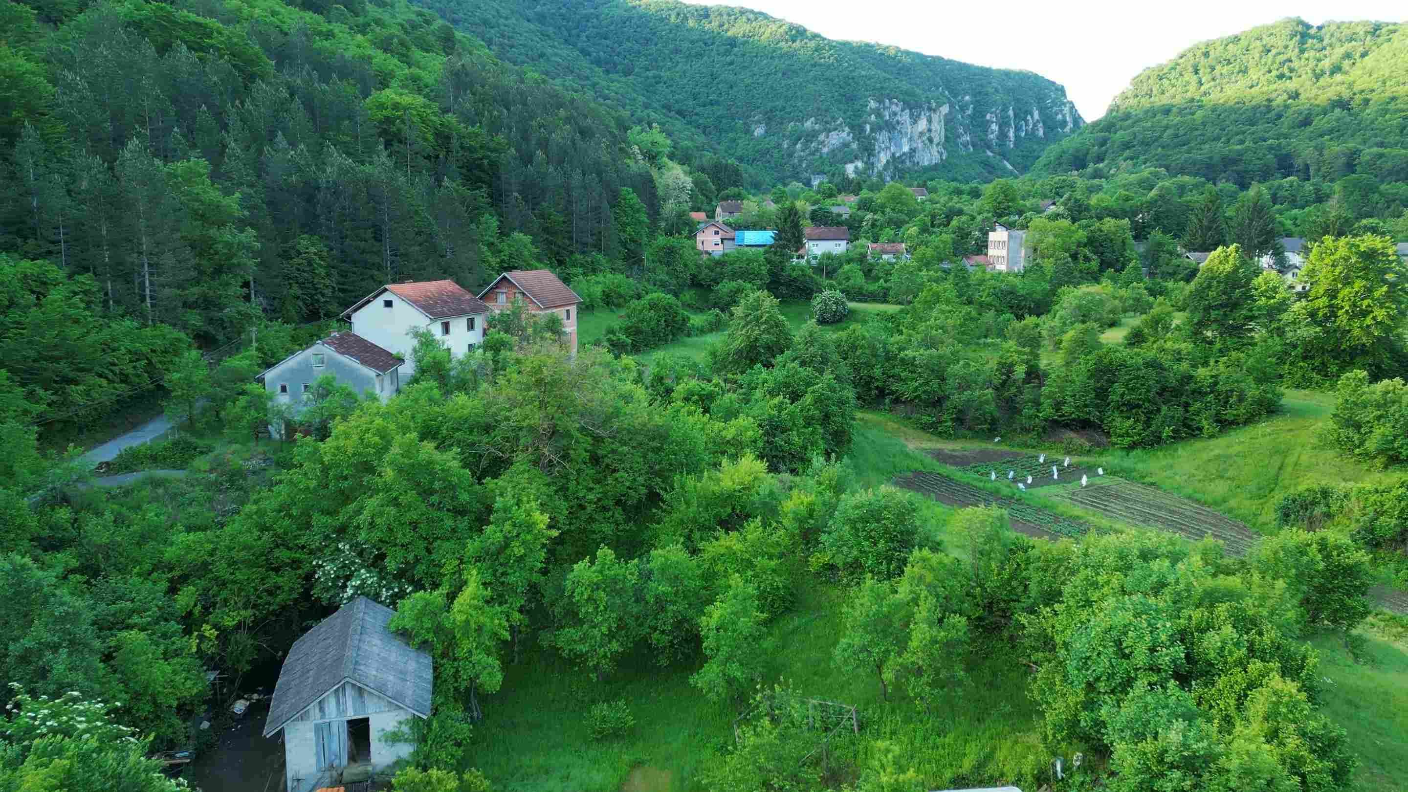 Pogled iz zraka na Martin Brod, kuće, zelene brežuljke i šumovitu dolinu.