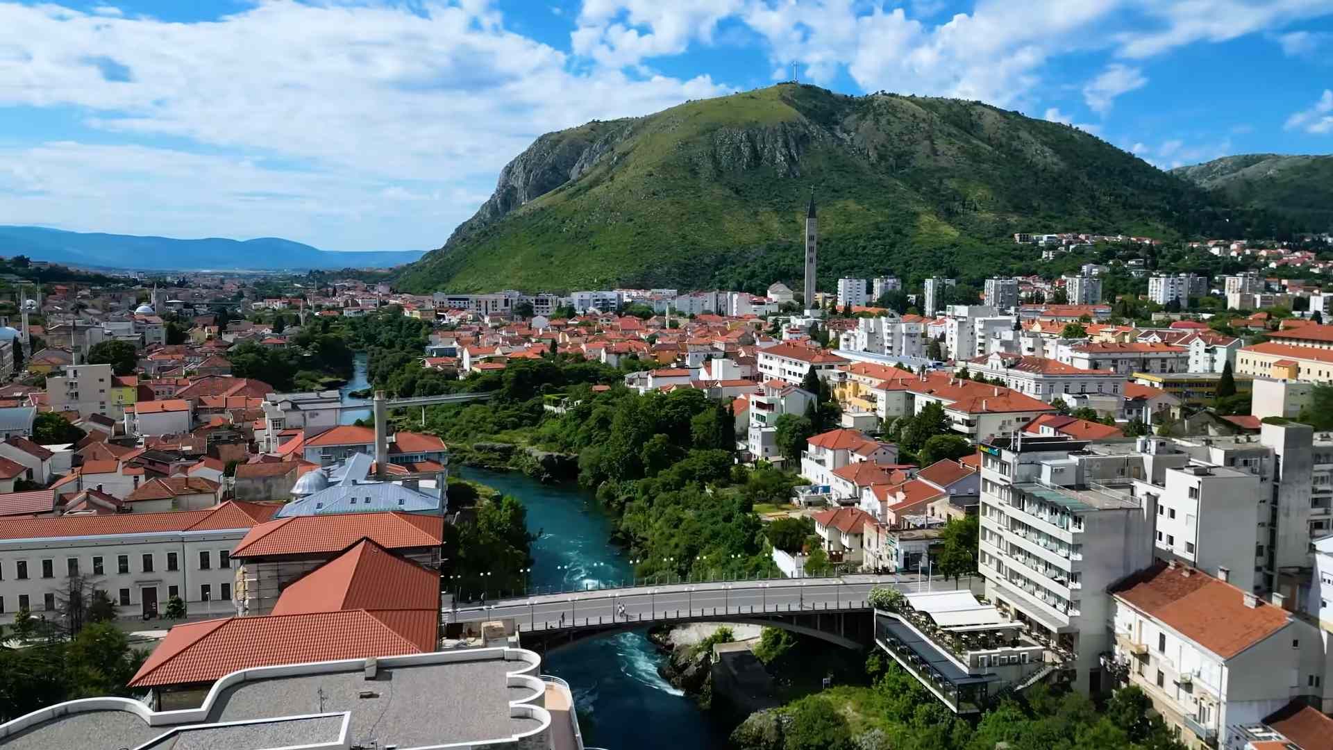 Panoramski pogled na Mostar, rijeku Neretvu, gradske mostove i okolne planine.
