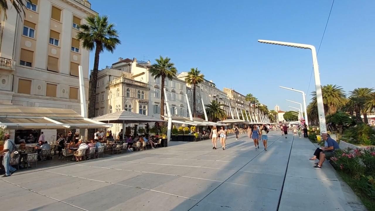 Splitska Riva s palmama, kafićima i turistima tijekom sunčanog dana.