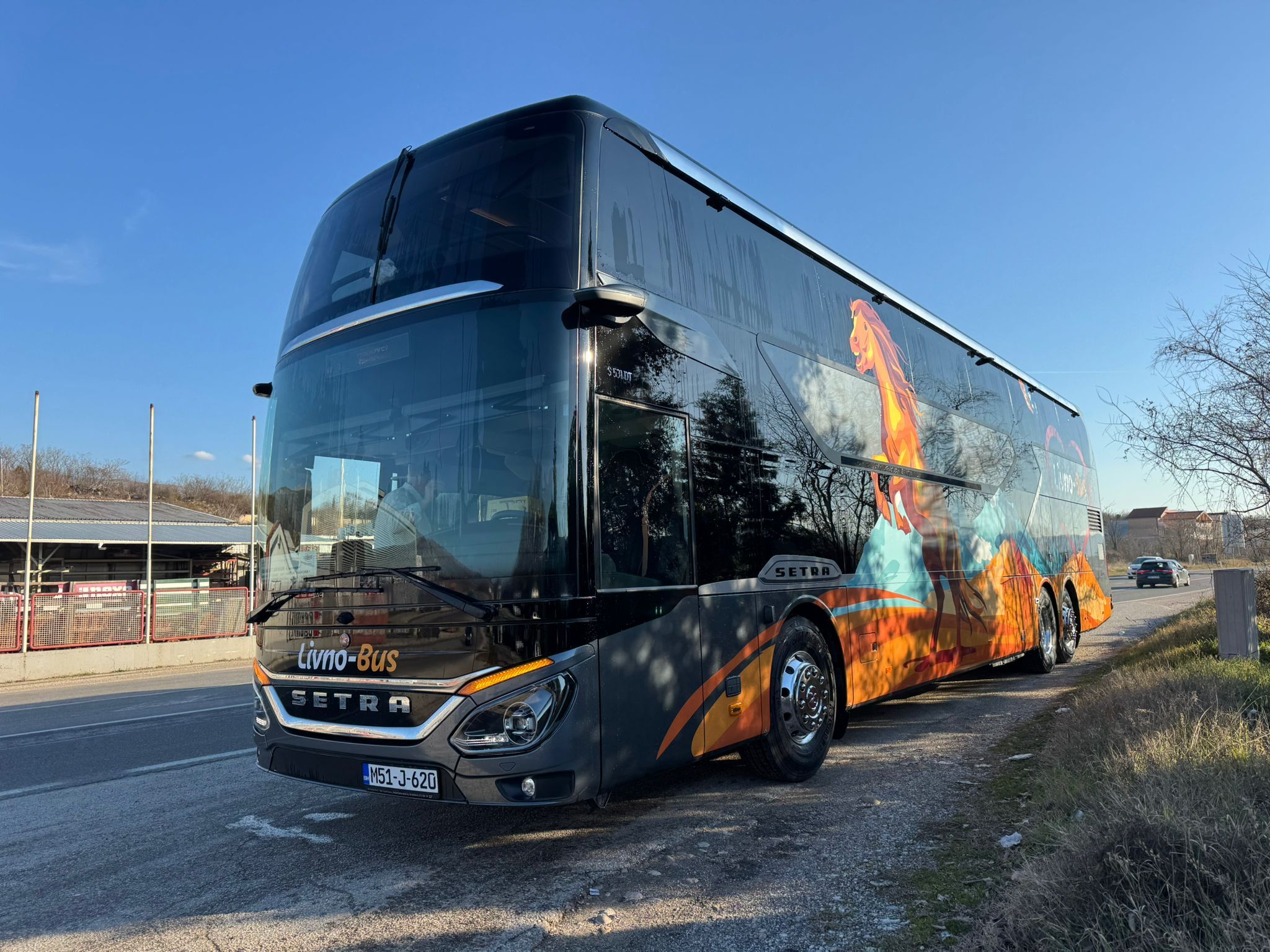 Moderni dvokatni autobus Livno-Bus parkiran uz cestu na sunčan dan, s prepoznatljivom grafikom konja i planinskog krajolika na bočnoj strani