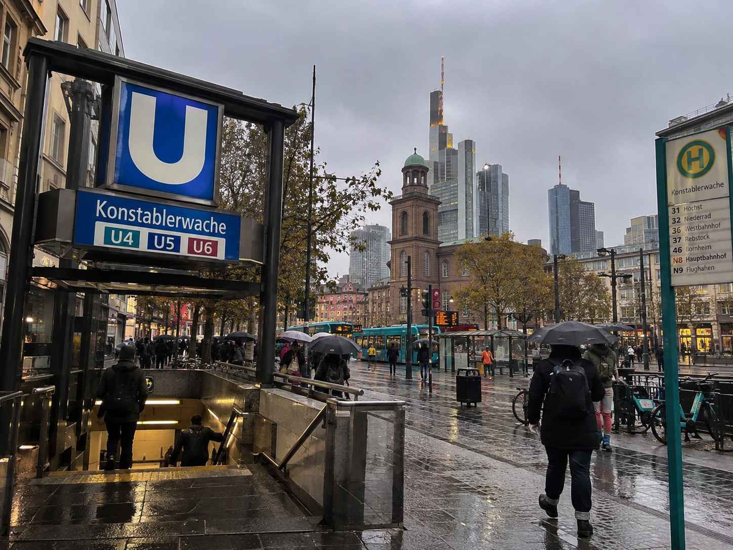 Kišni dan u Frankfurtu, ulaz u stanicu Konstablerwache i prolaznici s kišobranima.