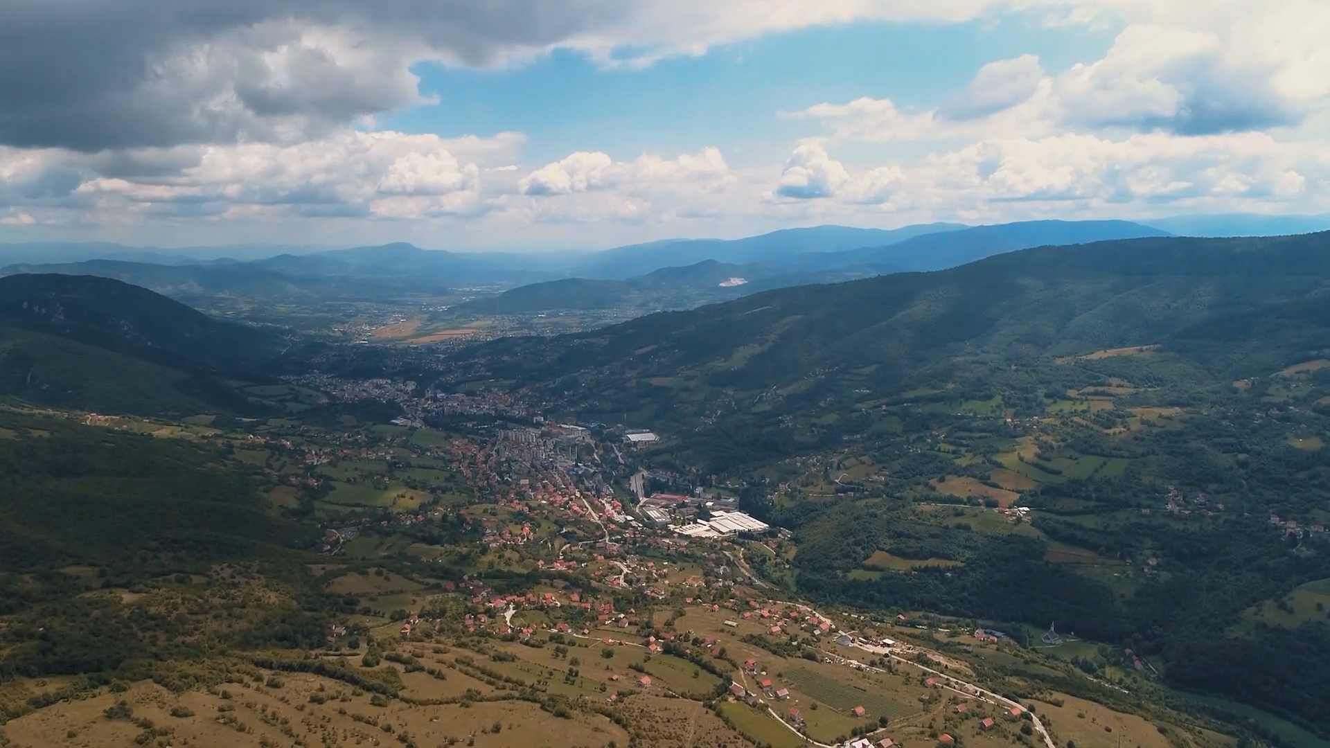 Panoramski pogled na planinu Vlašić, zelene doline i okolna naselja pod oblačnim nebom.